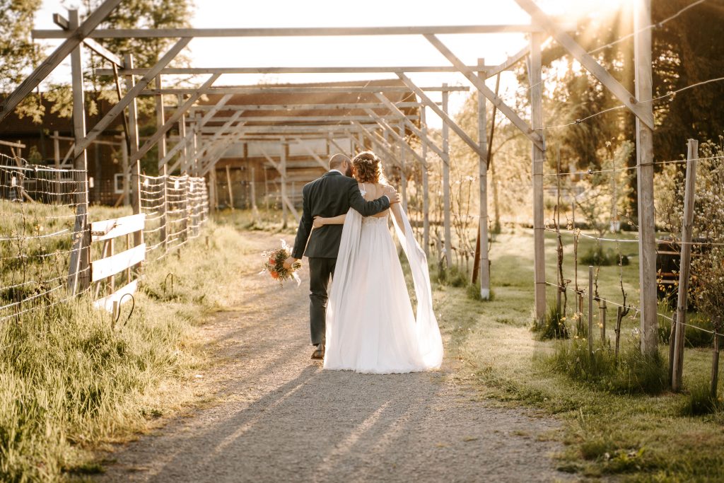 Brautpaar läuft Arm in Arm durch Laubengang bei Scheunenhochzeit in Baden-Württemberg.